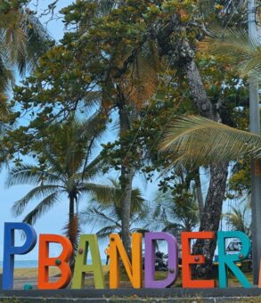 Letrero de Playa Bandera en Parrita, Costa Rica, con palmeras y bandera nacional