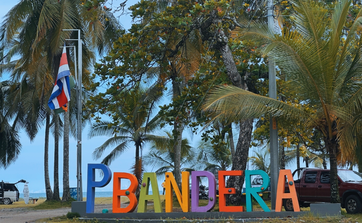 Letrero de Playa Bandera en Parrita, Costa Rica, con palmeras y bandera nacional
